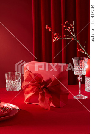 Front view photo about asian new year concept. Table setting for new year celebration with a red gift box placed in center, Tet's items decorated around, red curtain in back on red background 121417234