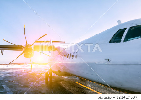 A close-up of the fuselage of a white passenger turboprop aircraft on the winter airport apron in the rays of the winter sun A close-up of the fuselage of a white passenger turboprop aircraft on the winter airport apron in the rays of the winter sun 121417337