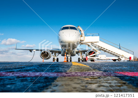Front view of white passenger airplane with a boarding steps at the airport apron 121417351