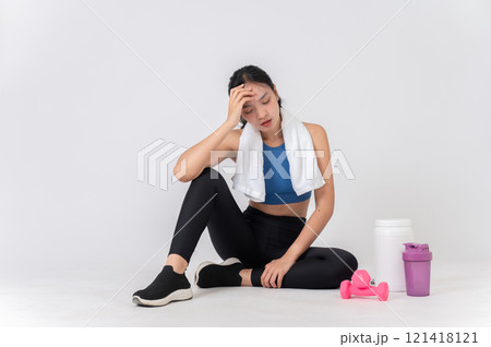 Tired Asian woman in sportswear sits on a studio background, taking a break after an intense workout Tired Asian woman in sportswear sits on a studio background, taking a break after an intense workout 121418121
