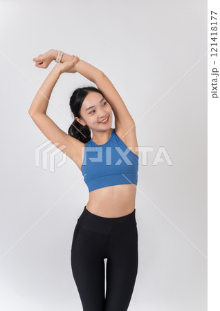 A beautiful, healthy Asian woman in sportswear stretching her arms and body, studio background. 121418177