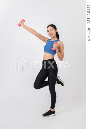 A cheerful young Asian woman in sportswear holding pink dumbbells on a white studio background. 121418182