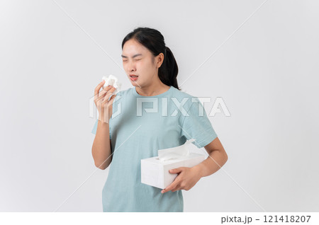 A sick Asian woman holding a tissue box, sneezing and blowing her nose, suffering from a runny nose. A sick Asian woman holding a tissue box, sneezing and blowing her nose, suffering from a runny nose. 121418207