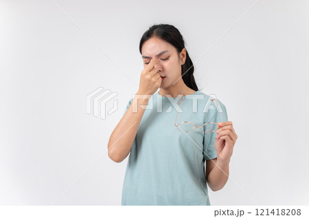 A tired, upset Asian woman taking off her glasses, suffering from eye strain, studio background. A tired, upset Asian woman taking off her glasses, suffering from eye strain, studio background. 121418208