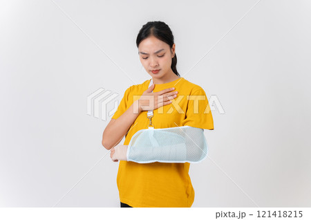 A sad Asian woman with a broken arm wrapped in a plaster bandage, wearing a sling to support her arm 121418215