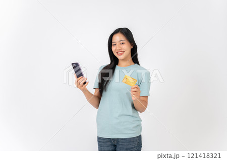 An Asian woman standing against a white studio background, holding a smartphone and a credit card. 121418321