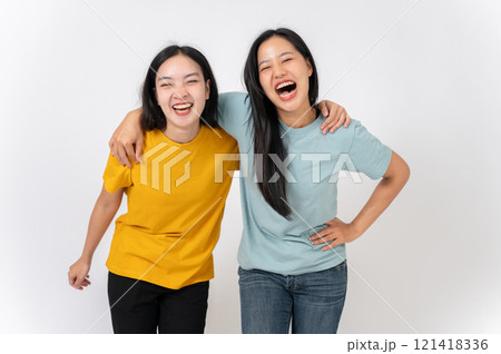 Two cheerful Asian female best friends standing against a white studio background, smiling with joy. 121418336