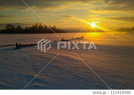Wonderful winter landscape during an amazing sunset with a country road, passing near the snow-covered fence in full growth. In the background are seen thickets of wild willow 121418500