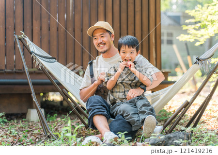 キャンプ場・アウトドア・レジャーでハンモックに座る父親と息子・男の子 キャンプ場・アウトドア・レジャーでハンモックに座る父親と息子・男の子 121419216