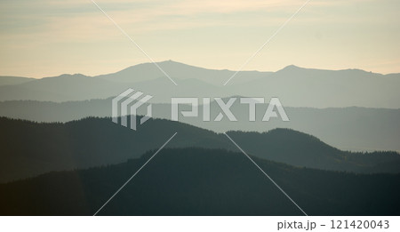 Mesmerizing view of layered mountain ranges in soft shades of green and gray, creating a sense of depth and tranquility under a subtle, misty sky. 121420043