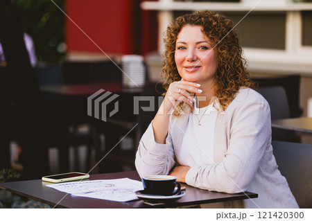 Woman sitting at an outdoor cafe. On the table are a smartphone, a coffee cup, and some papers Woman sitting at an outdoor cafe. On the table are a smartphone, a coffee cup, and some papers 121420300