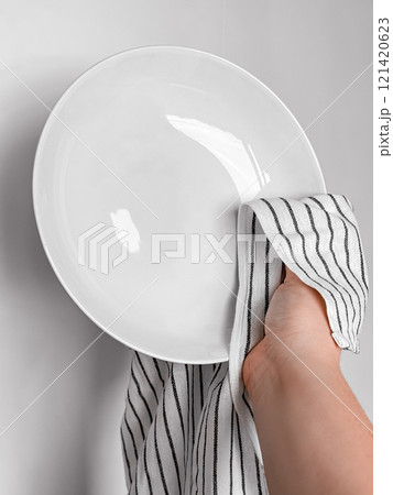 Hand drying white ceramic plate with striped cloth in kitchen setting Hand drying white ceramic plate with striped cloth in kitchen setting 121420623