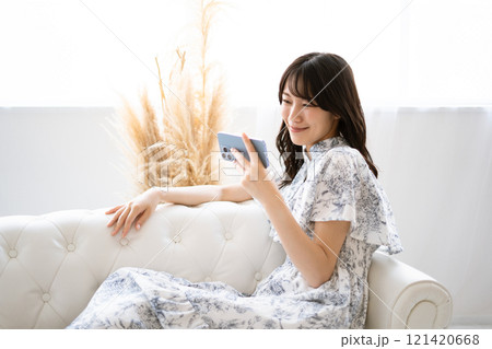 白いソファに座りスマホを持つ黒髪ロングヘアの若い女性 白いソファに座りスマホを持つ黒髪ロングヘアの若い女性 121420668