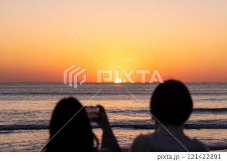 〈島根県〉稲佐の浜で海に沈む夕日を眺める観光客 121422891