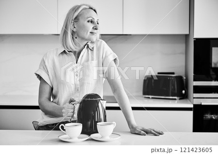 Pretty female making tea for two. Young woman holding kettle and brewing tea. Beautiful woman looking away and smiling. Black and white image. 121423605