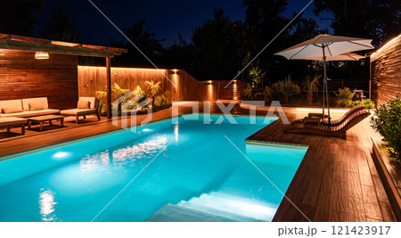 Luxury swimming pool with wooden deck and lounge area at night. Outdoor space with warm lighting and modern design 121423917