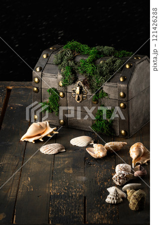 Decorative atmospheric pirate treasure chest covered with moss on an old wooden background and sea shells next to, vertical image, low key. Decorative atmospheric pirate treasure chest covered with moss on an old wooden background and sea shells next to, vertical image, low key. 121426288