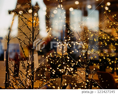 A garland of light bulbs glows behind a glass shop window before Christmas and New Year. Scandinavian supermarket chain with home and interior goods. Pula, Croatia - November 13, 2024 121427145