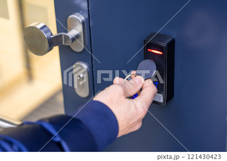 Close up view of person using a electric lock key fob to access a building via a reader of entry system mounted on a house wall 121430423