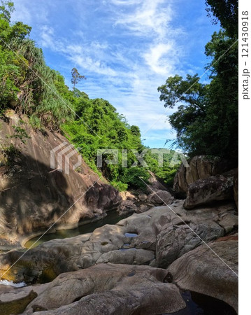 Vertical photo of huge stone boulders on a mountain river among dense forest and blue sky 121430918