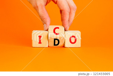 Initial coin or DEX offering symbol. Concept words abbreviation ICO or IDO on wooden block. Beautiful orange background. Businessman hand. Business Initial coin or DEX offering concept. Copy space. 121433005