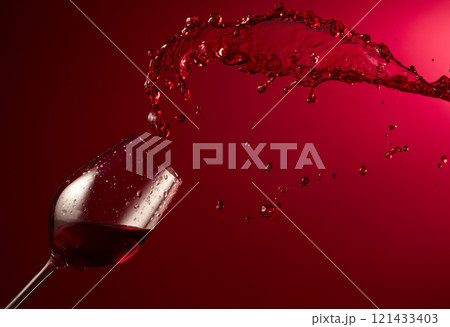 Glass and red wine splash on a dark red background. Glass and red wine splash on a dark red background. 121433403