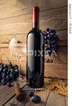 Bottle and glass of red wine with blue grapes on a wooden table. 121433406