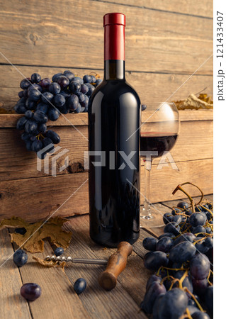 Bottle and glass of red wine with blue grapes on a wooden table. 121433407