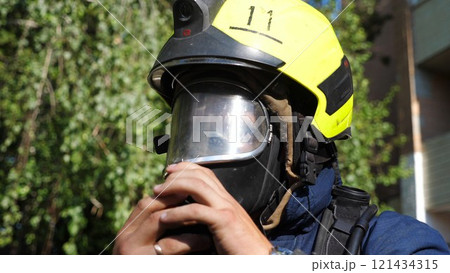 Young fireman connecting oxygen tank to the mask outdoor. Male fireguard in full equipment ready to extinguishing fire. Concept of saving lives and heroic profession. Close up Slow motion 121434315