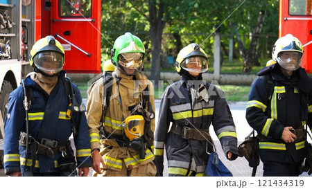 Tired male and female fireguards in full equipment walk after putting out the fire. Young exhausted firemen and firewoman go after extinguishing emergency. Saving lives and heroic profession concept 121434319