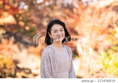 秋の公園を散策する笑顔のミドル女性 121436014