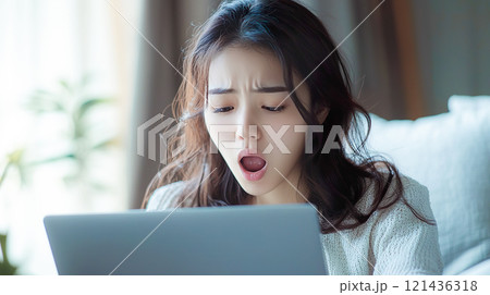 ノートパソコンの前で欠伸をする若い女性 121436318
