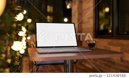 A close-up of a laptop on a table on an apartment balcony at night, illuminated by bulk lights. A close-up of a laptop on a table on an apartment balcony at night, illuminated by bulk lights. 121436588