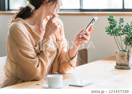カフェでコーヒーを飲みながらスマホを見る若いアジア人女性(待ち合わせ) カフェでコーヒーを飲みながらスマホを見る若いアジア人女性(待ち合わせ) 121437189