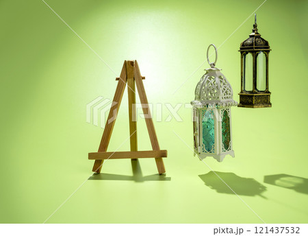 Wooden easel and Arabic lanterns hanging on a colored background. Decoration for Muslim holidays celebration Wooden easel and Arabic lanterns hanging on a colored background. Decoration for Muslim holidays celebration 121437532
