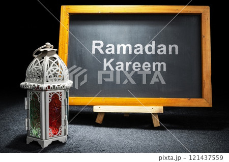 Wooden easel and chalkboard with the text of Ramadan Kareem and Arabic lantern on a black background Wooden easel and chalkboard with the text of Ramadan Kareem and Arabic lantern on a black background 121437559