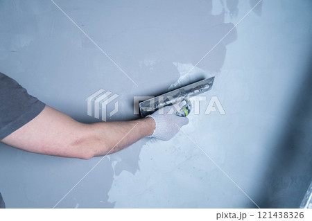 A worker uses a trowel to apply microcement adhesive to repair a wall in a residential area. 121438326