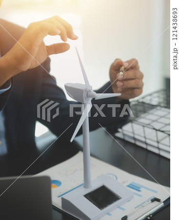 Shut of handsome business man working on new alternative energy development looking at a model of a wind turbine in modern startup. 121438693
