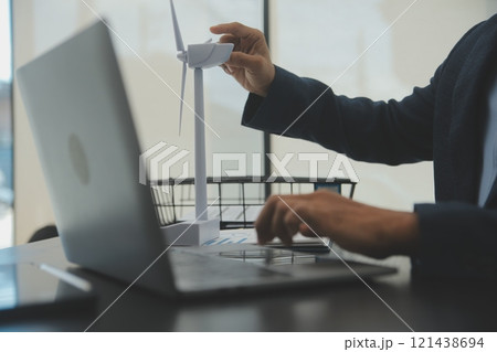 Shut of handsome business man working on new alternative energy development looking at a model of a wind turbine in modern startup. 121438694