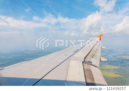 View of airplane wing, blue skies and green land during landing. Airplane window view. View of airplane wing, blue skies and green land during landing. Airplane window view. 121439257