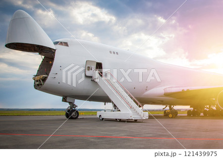 Unloading widebody cargo airplane at the airport apron in the morning sun. Freight aircraft bow compartment opened. Boarding steps at the plane 121439975