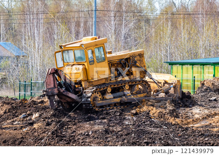 Yellow bulldozer leveling the ground at a construction site 121439979