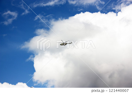 The helicopter flies against the background of a blue sky with clouds 121440007