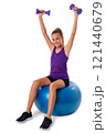 Slim and fit teen girl sitting a swiss blue ball and holding dumbbells with arms up. Isolated 121440679