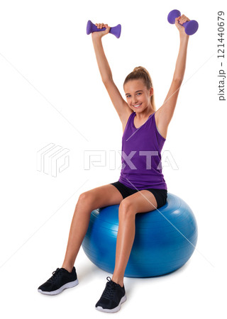 Slim and fit teen girl sitting a swiss blue ball and holding dumbbells with arms up. Isolated Slim and fit teen girl sitting a swiss blue ball and holding dumbbells with arms up. Isolated 121440679