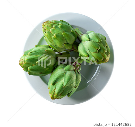 Green artichoke flower edible buds in a ceramic plate isolated on a white background. Top view. 121442685