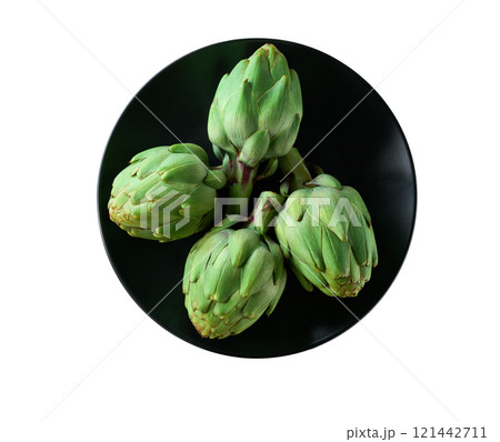 Fresh green artichoke in a black ceramic plate isolated on a white background. Top view. 121442711