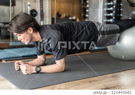 ジムでバランスボールを使いながらプランクで腹筋・体幹トレーニングをする若いアジア人男性 121443081