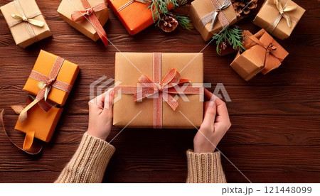 Hands grip a lovely wrapped gift amid other decorated presents and festive decor 121448099