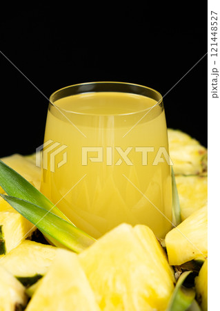 Pineapple juice in a glass among fresh pineapple fruit close-up. 121448527